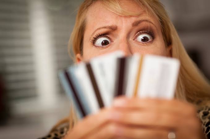 Uma mulher loira, visivelmente assustada, segurando 3 cartões de crédito na mão.
